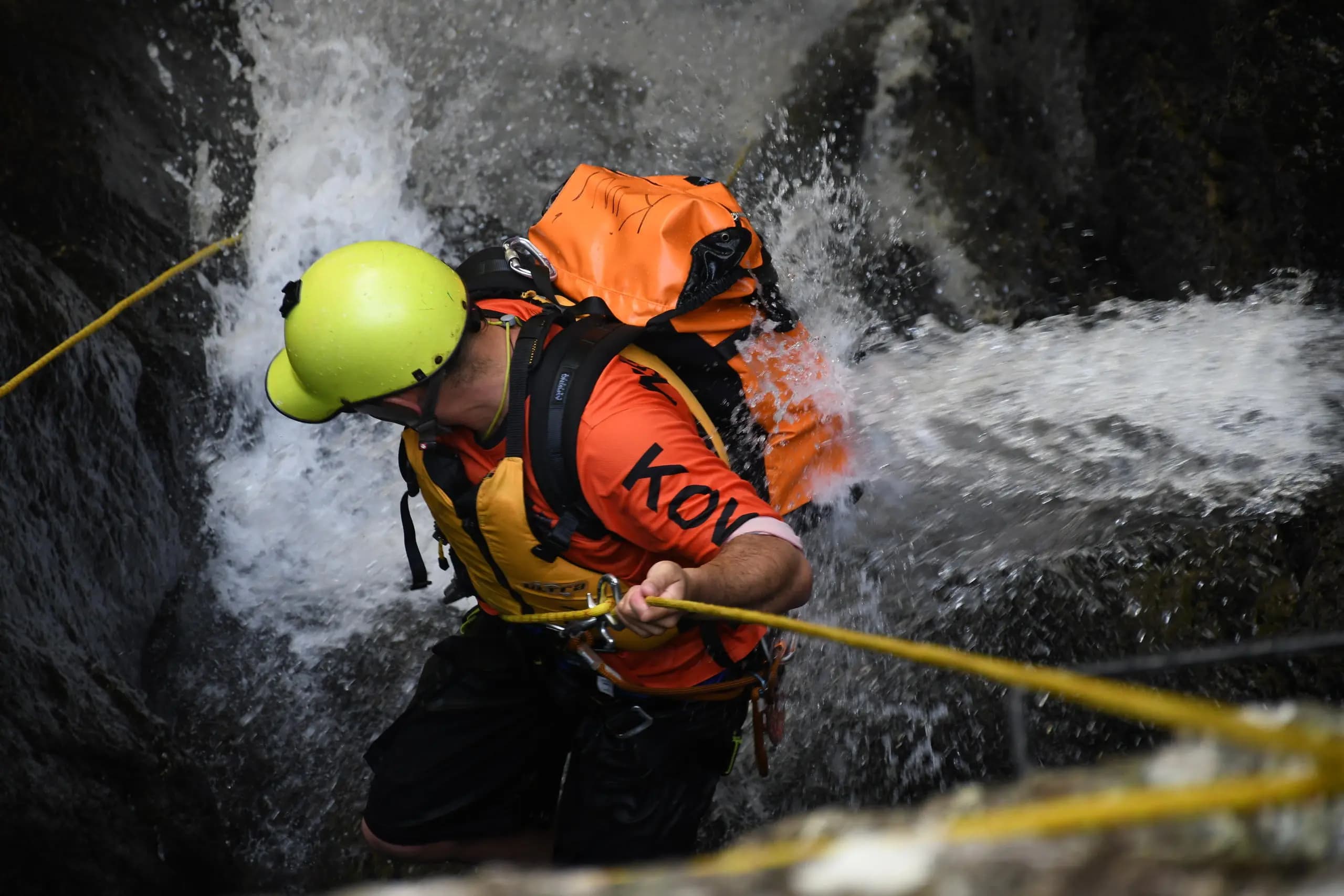 A person wearing a helmet and safety gear rappels down a rocky waterfall.